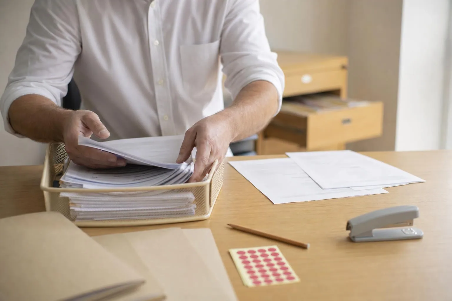Un responsable administratif trie une pile de contrats papier sortie d’une bannette métallique sur un plan de travail