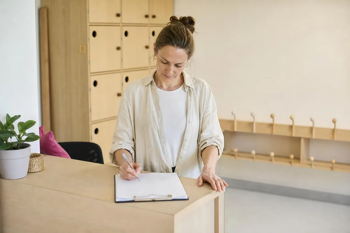 Directrice de multi accueil renseignant une feuille de presence papier sur le comptoir d’accueil de la structure